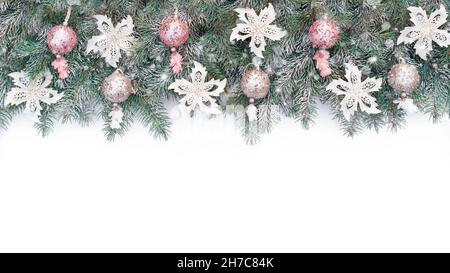 Weihnachtlicher Hintergrund mit einer Girlande aus Fichtenzweigen und Glitzerkugeln in Pink- und Champagnerfarben. Weihnachtsbanner in kalten Pastellfarben auf einem Whi Stockfoto