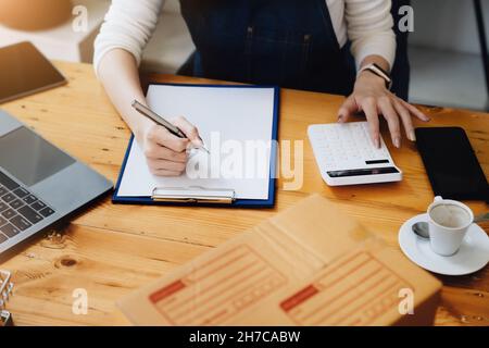 Unternehmer Besitzer mit Stift Punkt Notiz Laptop und Rechner Überprüfung Online-Kauf Bestellung zur Vorbereitung Pack Produkt Box. Verpacken von Waren für Stockfoto
