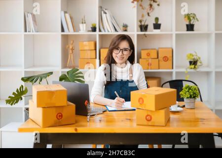 Unternehmer Besitzer mit Stift Punkt Notiz und Laptop Überprüfung Online-Kauf Bestellung zur Vorbereitung Pack Produkt Box. Verpacken von Waren für die Lieferung Stockfoto