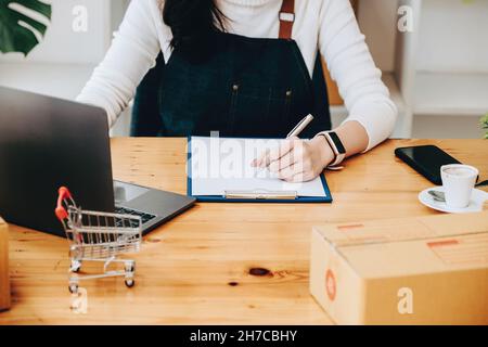 Unternehmer Besitzer mit Stift Punkt Notiz und Laptop Überprüfung Online-Kauf Bestellung zur Vorbereitung Pack Produkt Box. Verpacken von Waren für die Lieferung Stockfoto