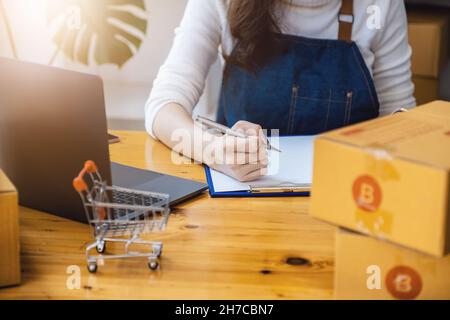 Unternehmer Besitzer mit Stift Punkt Notiz und Laptop Überprüfung Online-Kauf Bestellung zur Vorbereitung Pack Produkt Box. Verpacken von Waren für die Lieferung Stockfoto
