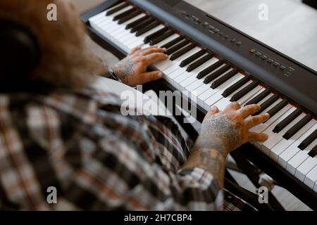 Komponist mit Übergewicht spielt Musik auf einem modernen Synthesizer, der im hellen Raum sitzt Stockfoto