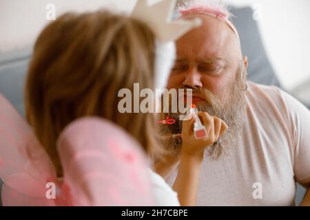 Blonde kleine Mädchen legt lipstic auf Vater Mund sitzt auf dem Sofa zu Hause Stockfoto