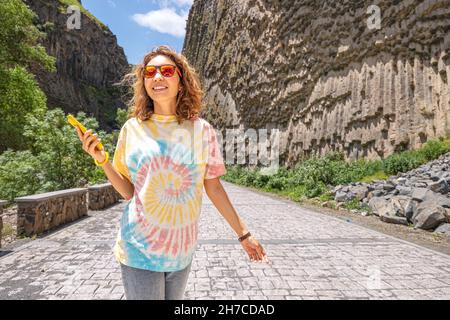 Eine Frau mit einem Smartphone geht entlang der Garni-Schlucht in Armenien mit den berühmten Basaltsäulen, die Sinfonie der Steine genannt werden Stockfoto