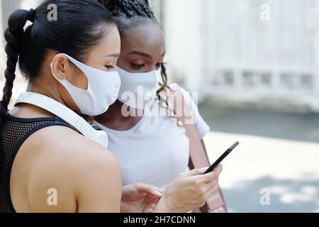 Junge Frau in Schutzmaske zeigt neue Sport-mobile Anwendung, um Freunde, wenn sie im Freien stehen Stockfoto