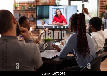 Diverse Geschäftsleute diskutieren Marketingstrategie mit Remote-Frau, die bei der Unternehmenspräsentation während der Online-Videocall-Konferenz im Startup-Office arbeitet. Geschäftsanruf auf dem Computerbildschirm Stockfoto