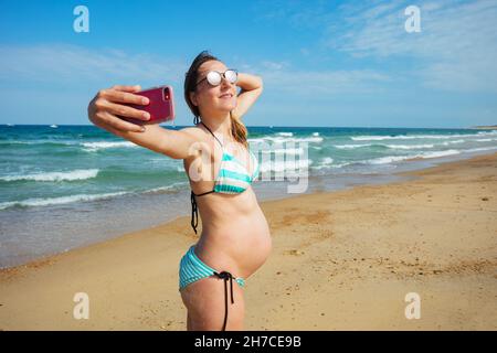 Eine Schwangerin im Urlaub nimmt Selfie am Strand Stockfoto
