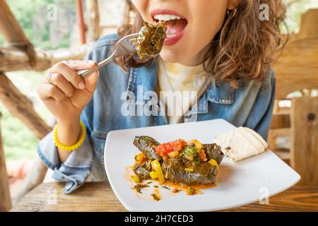 Happy Woman isst köstliche Dolma, ein traditionelles armenisches und georgisches Gericht aus Hackfleisch, das in Weintraubenblättern eingewickelt ist Stockfoto