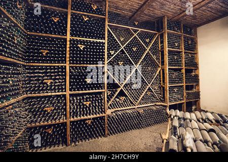 Regale mit veralterten Cognac-Flaschen, die mit Staub bedeckt sind, im Vintage-Weinkeller des alten Weinguts. Stockfoto