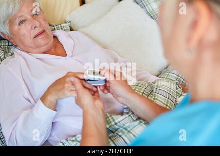 Geriatrische Krankenschwester misst den Puls einer kranken älteren Frau im Bett im Altersheim mit dem Pulsoximeter Stockfoto