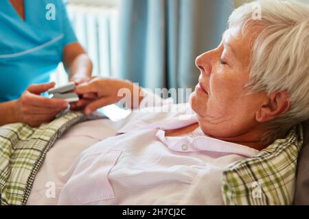 Die geriatrische Krankenschwester misst Puls und Sauerstoffsättigung bei kranken älteren Frauen im Bett im Pflegeheim Stockfoto
