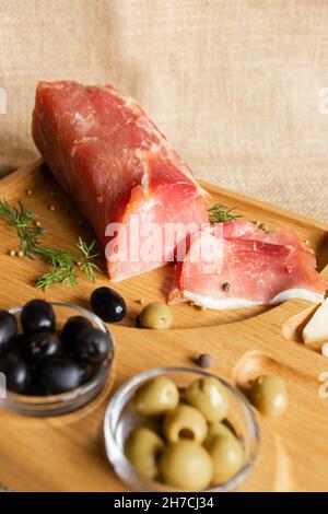 Getrocknete Schweinsfilet auf dem hölzernen Servierbrett mit Käse, Oliven, schwarzem Pfeffer, Tomatensauce. Jerky Filet Vorspeise. Gericht von Weißrussisch Stockfoto