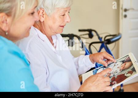 Demented ältere Frau zeigt geriatrische Krankenschwester Fotos von Enkelin als Baby-aif-Kalender Stockfoto