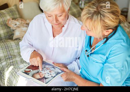 Eine alte Frau mit Demenz und eine Krankenschwester schauen sich zusammen ein Fotoalbum an Stockfoto