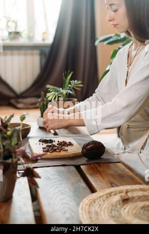 Frau Hände schälen Bio-Kakaobohnen auf Holztisch, Kakaobohnen, handwerkliche Schokolade in rustikalem Stil für die Zeremonie auf dem Tisch. Degustation Stockfoto