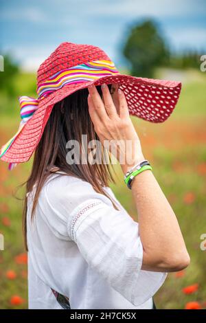 Schöne Frau trägt Strohhut genießen den Blick auf eine Mohnwiese im Frühjahr Saison Stockfoto