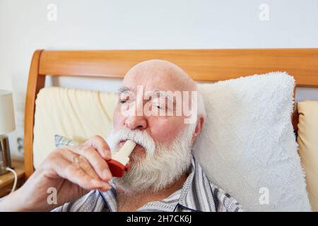 Senior im Bett mit chronischer Atemwegserkrankung verwendet Aerosol mit Asthmaspray Stockfoto