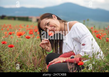 Frau schnüffelt in der Frühjahrssaison einen roten Mohns inmitten einer wunderschönen Mohnwiese Stockfoto