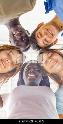 Blick nach oben auf Jugendliche, die im Kreis miteinander lächeln. Multi ethnische Freunde glücklich, Freundschaft und Antirassismus Konzept. Stockfoto