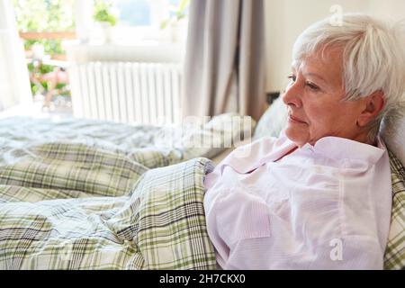 Kranke alte Frau im Bett als nachdenkliche Patientin zu Hause oder im Altersheim Stockfoto