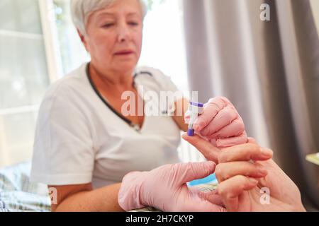 Krankenschwester oder Arzt, der den Blutzucker am Finger eines Patienten in einem Pflegeheim misst Stockfoto