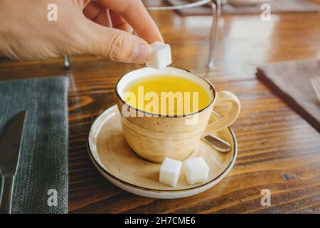 Ein Mann legt weißen raffinierten Zucker in grünen Kräutertee. Das Konzept von Diabetes und sucht nach schnellen Kohlenhydraten Stockfoto