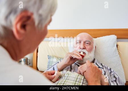 Senior im Krankenhausbett verwendet Asthmaspray mit Unterstützung der geriatrischen Krankenschwester Stockfoto