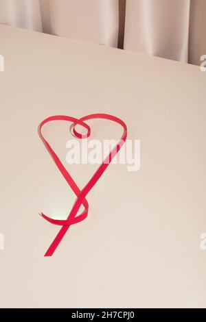 Trendige, minimalistische Komposition zum Valentinstag mit rotem Herzband auf elegentem Seidenhintergrund. Modernes Liebeskonzept. Stockfoto