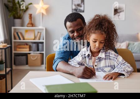 Porträt eines fürsorglichen afroamerikanischen Vaters, der Hausaufgaben mit seiner Tochter zu Hause macht, Platz kopieren Stockfoto
