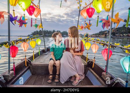 Glückliche Familie Mutter und Sohn von Reisenden reiten auf einem Nationalboot auf dem Hintergrund der alten Stadt Hoi, Vietnam. Vietnam öffnet sich danach wieder für Touristen Stockfoto