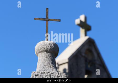 Nahaufnahme eines rostigen eisernen christlichen Kreuzes auf einer Säule und einem Kirchturm im Hintergrund. Religion, christentum, Architektur und Geschichtskonzepte Stockfoto