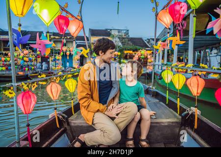 Glückliche Familie Vater und Sohn von Reisenden fahren ein nationales Boot auf dem Hintergrund von Hoi an alten Stadt, Vietnam. Vietnam öffnet sich danach wieder für Touristen Stockfoto