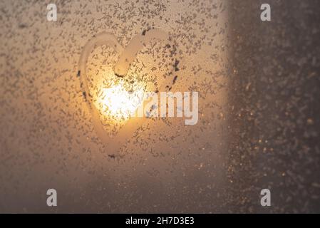 Ein Herz gezeichnet auf einem gefrorenen Winterfenster bei Sonnenuntergang. Stockfoto