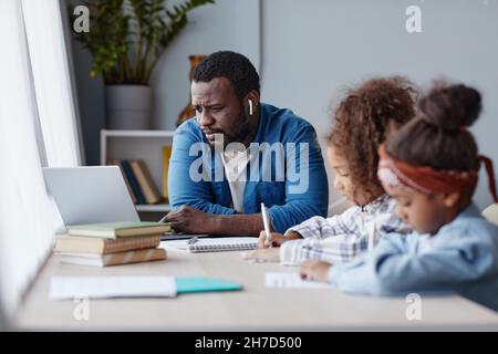 Porträt des fürsorglichen Vaters, der Hausaufgaben mit zwei kleinen Mädchen in der Online-Schule zu Hause macht, Platz kopieren Stockfoto