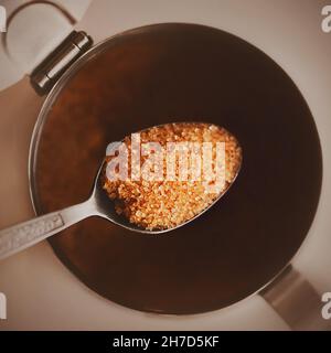 Draufsicht auf einen eleganten Teelöffel mit Mustern, bei dem eine Portion Zuckerrohr gesunden Zucker braun, der aus der Zuckerschale entnommen wird. Richtige Ernährung. Stockfoto