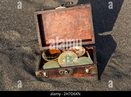 Münzen verschiedener Kryptowährungen in einer Schatzkiste am Strand Stockfoto