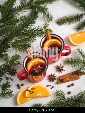 Glühwein in zwei roten Tassen auf einem Weihnachtstisch, umgeben von Zweigen aus Tanne, Orangen und Gewürzen Stockfoto