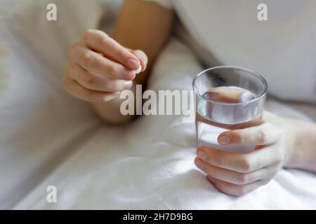 Ein kranker junger Mann hält eine Pille und ein Glas Wasser in der Hand Stockfoto