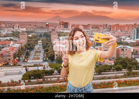 Eine glückliche Asiatin macht ein Selfie-Foto für ihren Reise-Blog in sozialen Netzwerken vor dem Hintergrund der Hauptstadt Armeniens - Jerewan und M Stockfoto