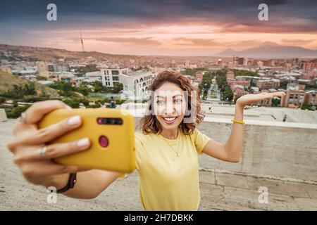 Eine glückliche Asiatin macht ein Selfie-Foto für ihren Reise-Blog in sozialen Netzwerken vor dem Hintergrund der Hauptstadt Armeniens - Jerewan und M Stockfoto