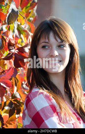 Ein junges hübsches Mädchen mit langen schwarzen Haaren geht im Park um die gelben Blätter der Bäume herum. Die Frau ist in einem sportlichen Stil gekleidet. Freude, Herbst, so Stockfoto