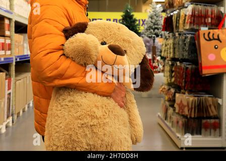 Ein Mann kaufte einen großen Teddybären im Laden, ein Geschenk für ein Kind zu seinem Geburtstag, Weihnachten, Neujahr. Weihnachtseinkäufe im Einkaufszentrum, Geschäft, Supermarkt Stockfoto