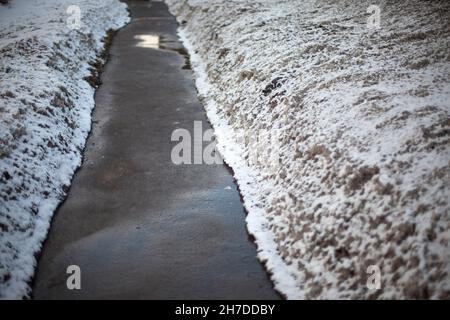 Der Weg ist schneefrei. Schmale Spur zwischen Schneeverwehungen. Asphalt im Winter. Stockfoto