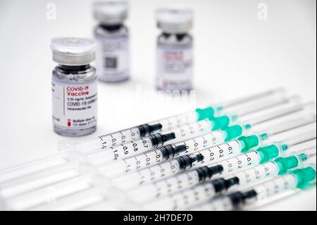 Coronavirus-Impfung gegen SARS-CoV-2 – medizinische Spritzen, jeweils mit einer Dosis COVID-19-Impfstoff, und mehrere Glasfläschchen im Hintergrund. Stockfoto