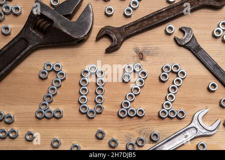 Die Nummern 2022 sind auf einem Holztisch neben einer Vielzahl von Schraubenschlüsseln mit Metallmuttern ausgekleidet. Konzept des Beginns des neuen Jahres. Draufsicht. Stockfoto