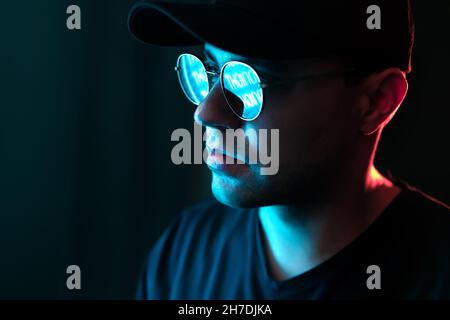 Mann mit Neonlicht auf Brille und Gesicht. Blaue und rote Farbe von der Stadt-Plakatwand im dunklen Studioportrait. Spiegelung in Sonnenbrillen. Schwarzer Hintergrund. Stockfoto