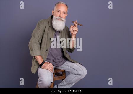 Foto von pensionierten brutalen Mann ruhen Sessel genießen Rauchen lässige Outfit isoliert über grauen Hintergrund Stockfoto