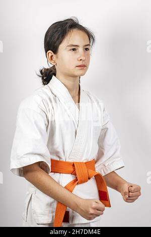 Karate Mädchen auf einem weißen Hintergrund. Sportliche kaukasische Brünette in einem weißen Kimono mit einem orangen Gürtel. Kontaktieren Sie den Sport. Orientalische Kampfkünste gesunde LIF Stockfoto