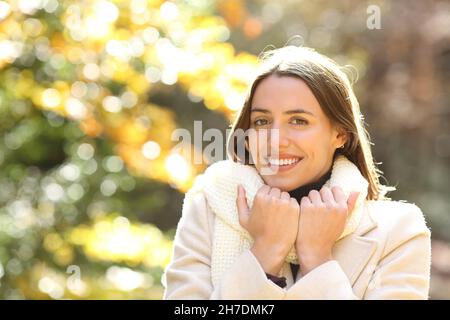 Glückliche Frau, die in einem Park warm gekleidet ist und die Kamera anschaut Stockfoto