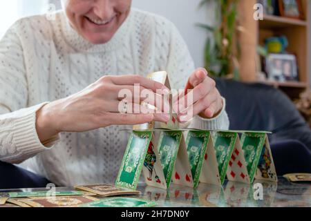 Hände einer Frau, die einen Turm aus Spielkarten stapelt. Nahaufnahme. Selektiver Fokus. Bewegungsunschärfe. Stockfoto